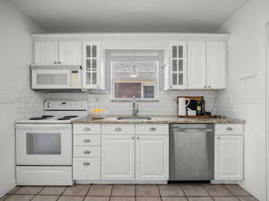 Kitchen featuring white appliances, white cabinetry, light tile patterned floors, glass insert cabinets, and tasteful backsplash