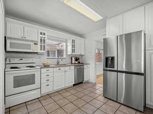 Kitchen with stainless steel appliances, white cabinets, glass insert cabinets, backsplash, and light tile patterned floors