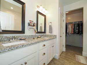 Bathroom featuring wood finished floors, a walk in closet, double vanity, baseboards, and recessed lighting