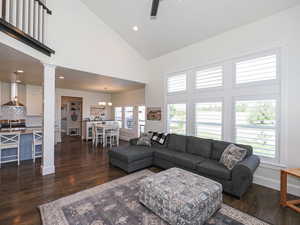 Living area with high vaulted ceiling, dark wood finished floors, decorative columns, baseboards, and a ceiling fan