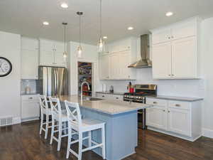 Kitchen with appliances with stainless steel finishes, wall chimney range hood, a sink, dark wood-type flooring, and white cabinetry
