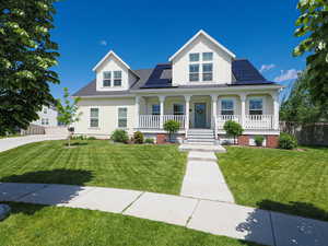 View of front facade with a porch, roof mounted solar panels, roof with shingles, and board and batten siding