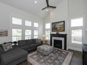 Living area featuring high vaulted ceiling, dark wood-style floors, ceiling fan, a premium fireplace, and baseboards