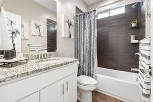Bathroom featuring wood finished floors, toilet, shower / tub combo with curtain, and vanity