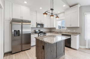 Kitchen with appliances with stainless steel finishes, a sink, light wood finished floors, white cabinetry, and recessed lighting
