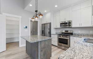 Kitchen featuring appliances with stainless steel finishes, light wood-style flooring, white cabinetry, decorative light fixtures, and recessed lighting