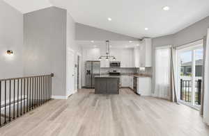 Kitchen featuring appliances with stainless steel finishes, vaulted ceiling, white cabinetry, light wood finished floors, and a center island