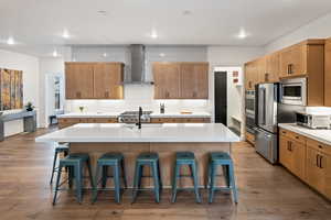 Kitchen with wall chimney exhaust hood, appliances with stainless steel finishes, a kitchen bar, an island with sink, and recessed lighting