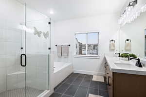 Bathroom featuring tile patterned flooring, a bath, a shower stall, baseboards, and double vanity