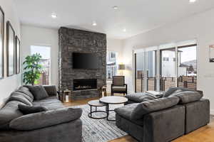 Living area with light wood-type flooring, a stone fireplace, baseboards, and recessed lighting
