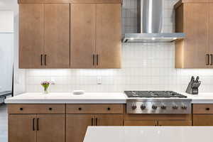 Kitchen featuring wall chimney exhaust hood, stainless steel gas cooktop, light countertops, and decorative backsplash