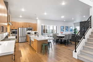 Kitchen featuring appliances with stainless steel finishes, open floor plan, a breakfast bar, light countertops, and light wood finished floors