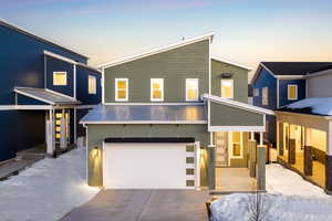 Contemporary home featuring a garage, driveway, stucco siding, and metal roof