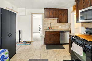 Kitchen with appliances with stainless steel finishes, a sink, light stone counters, and backsplash