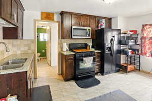 Kitchen featuring black appliances, a sink, backsplash, dark brown cabinets, and light stone counters