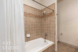 Full bath with shower / tub combo with curtain, tile patterned floors, toilet, and baseboards