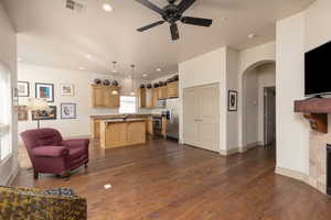Living area featuring arched walkways, recessed lighting, ceiling fan, dark wood-type flooring, and a tiled fireplace