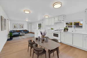 Kitchen featuring white appliances, a sink, under cabinet range hood, light countertops, and light wood-type flooring