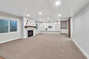 Unfurnished living room featuring light colored carpet, baseboards, recessed lighting, a barn door, and a fireplace