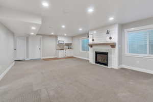 Unfurnished living room with light colored carpet, a fireplace, baseboards, and recessed lighting