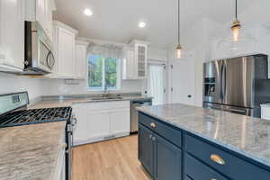 Kitchen with stainless steel appliances, a sink, white cabinets, blue cabinetry, and tasteful backsplash