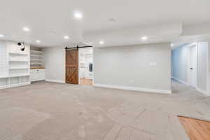 Below grade area with a barn door, recessed lighting, baseboards, light carpet, and washer / clothes dryer