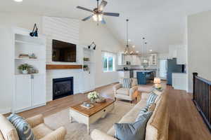 Living area with high vaulted ceiling, light wood-style floors, ceiling fan, a fireplace, and baseboards
