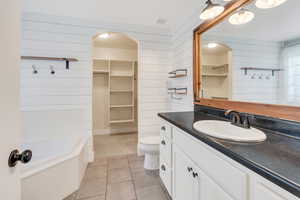 Bathroom with wood walls, tile patterned floors, a spacious closet, toilet, and vanity