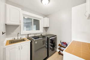 Laundry room featuring washer and clothes dryer, cabinet space, light wood finished floors, and a textured ceiling