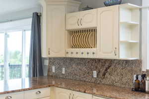 Kitchen featuring open shelves, decorative backsplash, and dark stone countertops
