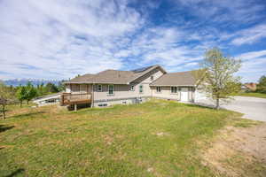 Rear view of house with a yard, roof mounted solar panels, a wooden deck, stucco siding, and central AC