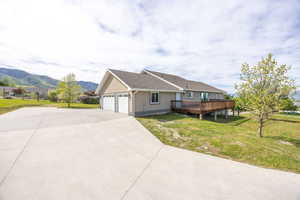 View of side of home featuring a deck with mountain view, a lawn, driveway, a garage, and stucco siding