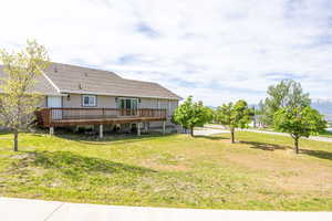 Back of property with a wooden deck, a lawn, and roof with shingles