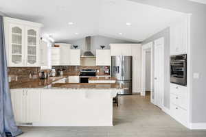 Kitchen with appliances with stainless steel finishes, wall chimney exhaust hood, a peninsula, lofted ceiling, and open shelves