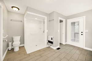 Full bathroom with heating unit, wood tiled floors, a shower stall, and baseboards