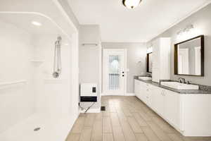 Full bathroom featuring heating unit, double vanity, wood finished floors, a shower, and baseboards