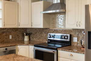 Kitchen featuring appliances with stainless steel finishes, wall chimney exhaust hood, tasteful backsplash, and white cabinets