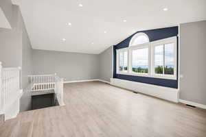 Unfurnished living room with vaulted ceiling, wood finished floors, baseboards, and recessed lighting