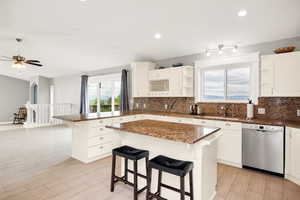 Kitchen with stainless steel dishwasher, open shelves, a peninsula, a breakfast bar, and tasteful backsplash