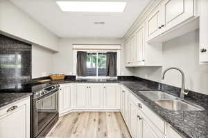 Kitchen featuring electric stove, a sink, light wood-type flooring, dark stone countertops, and white cabinets