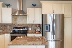 Kitchen featuring stainless steel appliances, wall chimney exhaust hood, tasteful backsplash, and dark stone counters