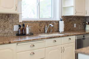 Kitchen with stainless steel dishwasher, a sink, open shelves, white cabinetry, and backsplash