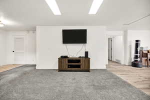Unfurnished living room featuring attic access, baseboards, carpet flooring, and wood finished floors