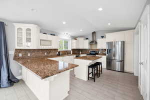 Kitchen with appliances with stainless steel finishes, wall chimney exhaust hood, a kitchen bar, vaulted ceiling, and a sink