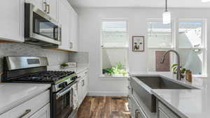 Kitchen with stainless steel appliances, decorative backsplash, dark wood-style flooring, a sink, and light countertops