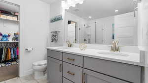 Bathroom with a shower stall, toilet, double vanity, recessed lighting, and baseboards