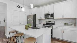 Kitchen with stainless steel appliances, wood finished floors, an island with sink, decorative backsplash, and a kitchen breakfast bar