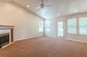 Unfurnished living room featuring healthy amount of natural light, light carpet, a ceiling fan, a textured ceiling, and vaulted ceiling