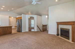 Unfurnished living room featuring light carpet, vaulted ceiling, a ceiling fan, arched walkways, and a tiled fireplace