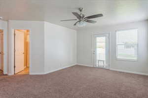 Empty room with light colored carpet, a ceiling fan, baseboards, and a textured ceiling